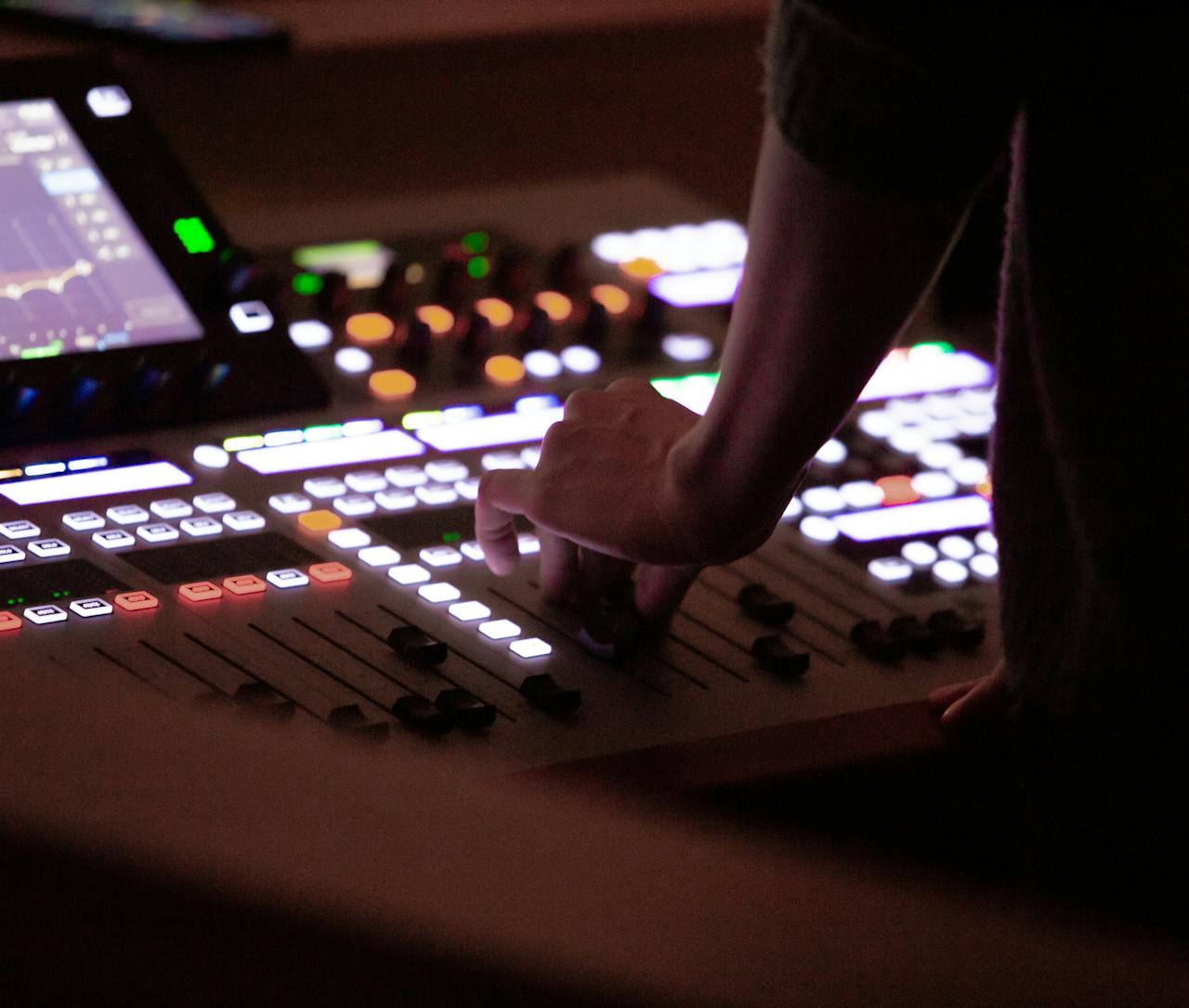 Sound engineer's hand adjusting mixer controls during an event. Dim lighting, focus on technology.